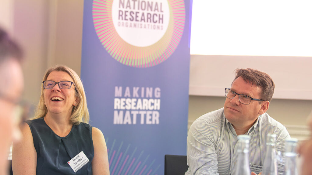 2 people sat in front of a banner that reads national research organisations.