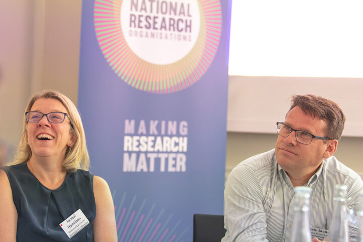 2 people sat in front of a banner that reads national research organisations.