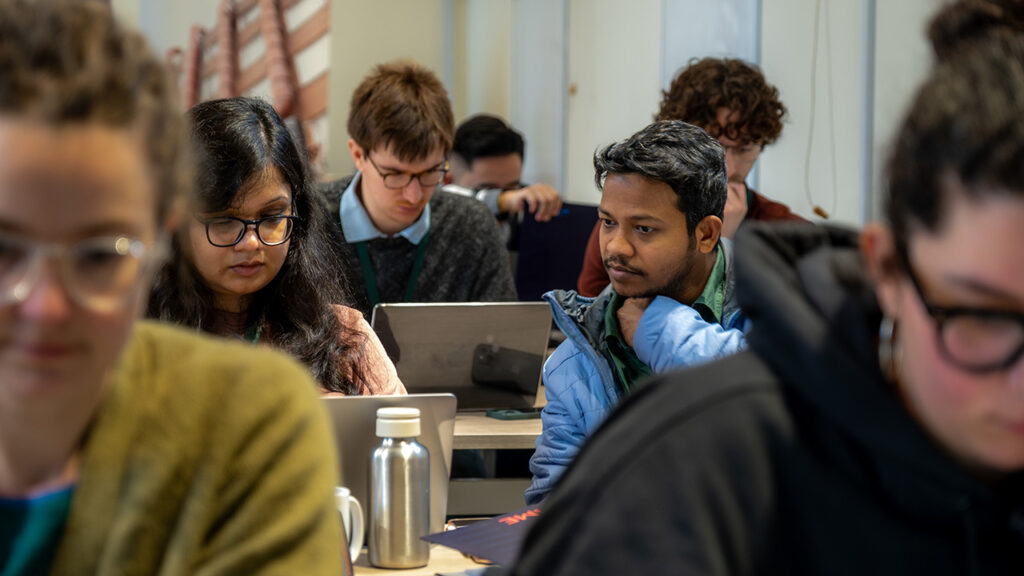 People sat in rows, working on laptops on tables, in a training room.
